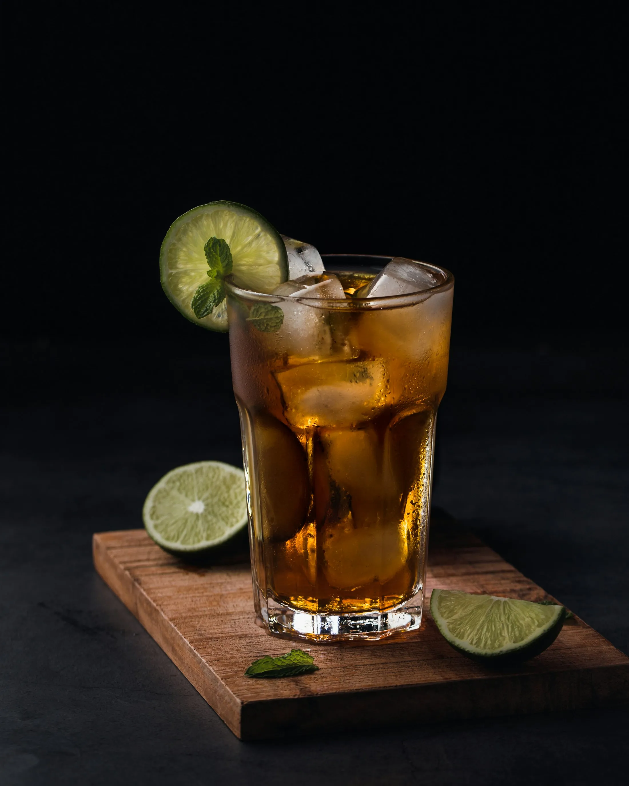A tall glass of iced black tea garnished with lime and mint on a wooden board