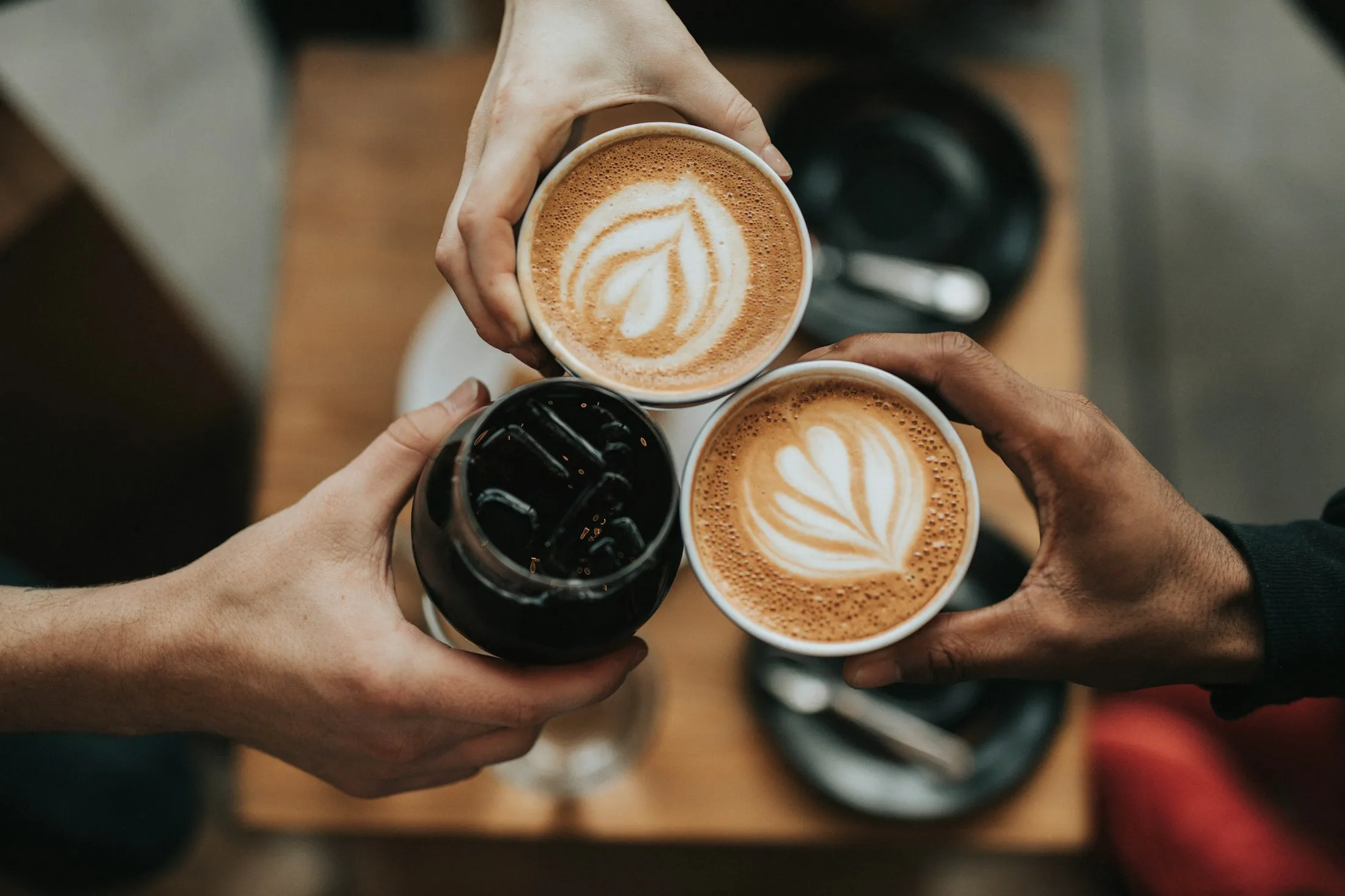 Three latte cups held aloft in a casual cheers