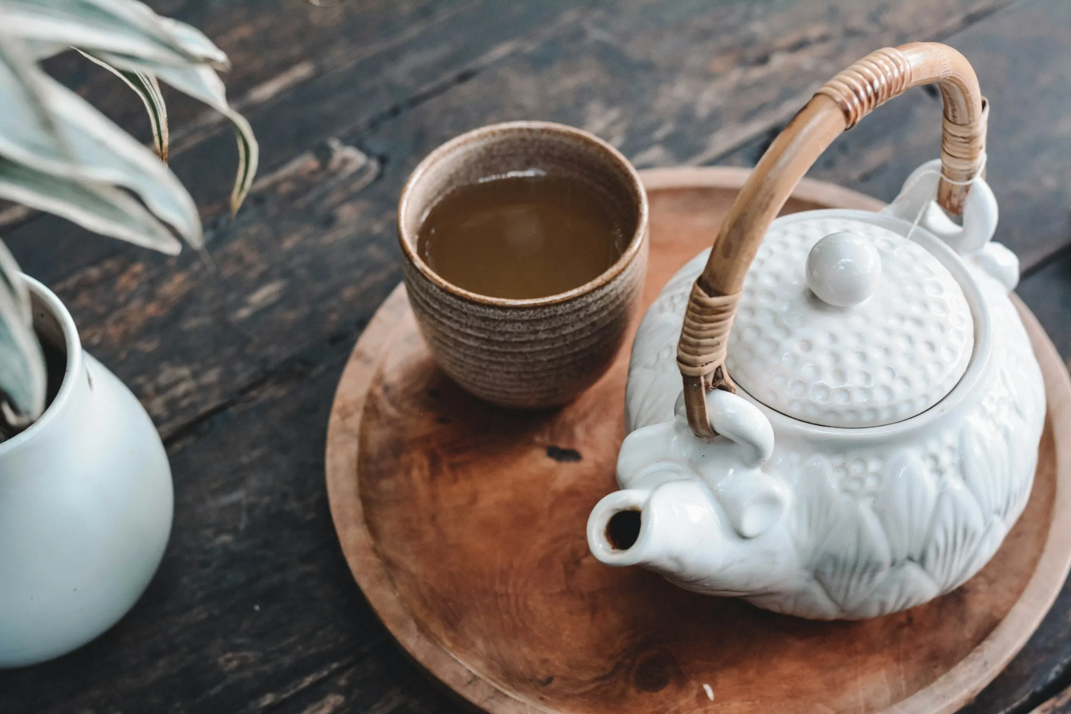 A small white teapot and a brown ceramic tea cup on a wooden tray