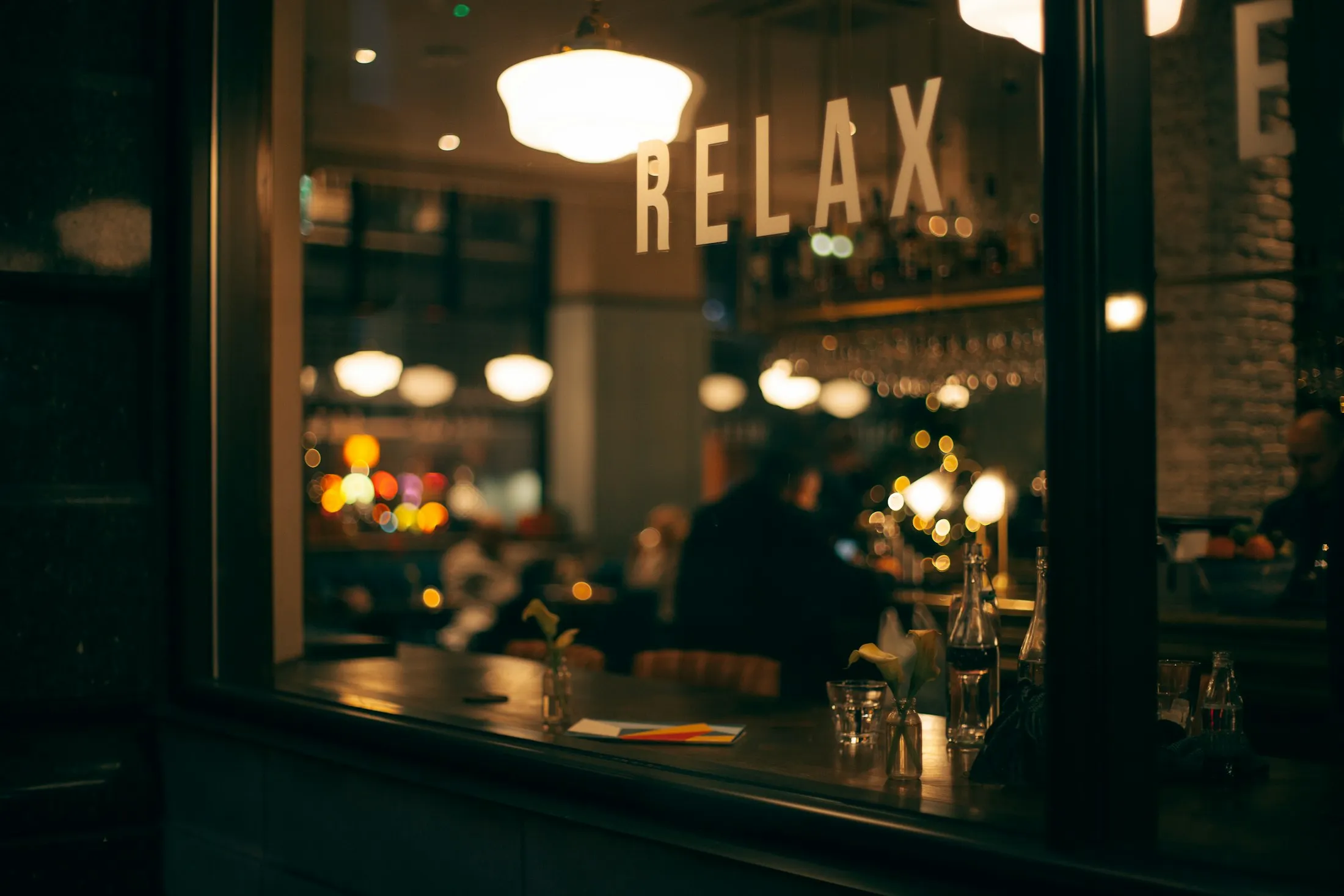 A warmly lit bar window inside the cafe at dusk with the word RELAX in serif on the glass