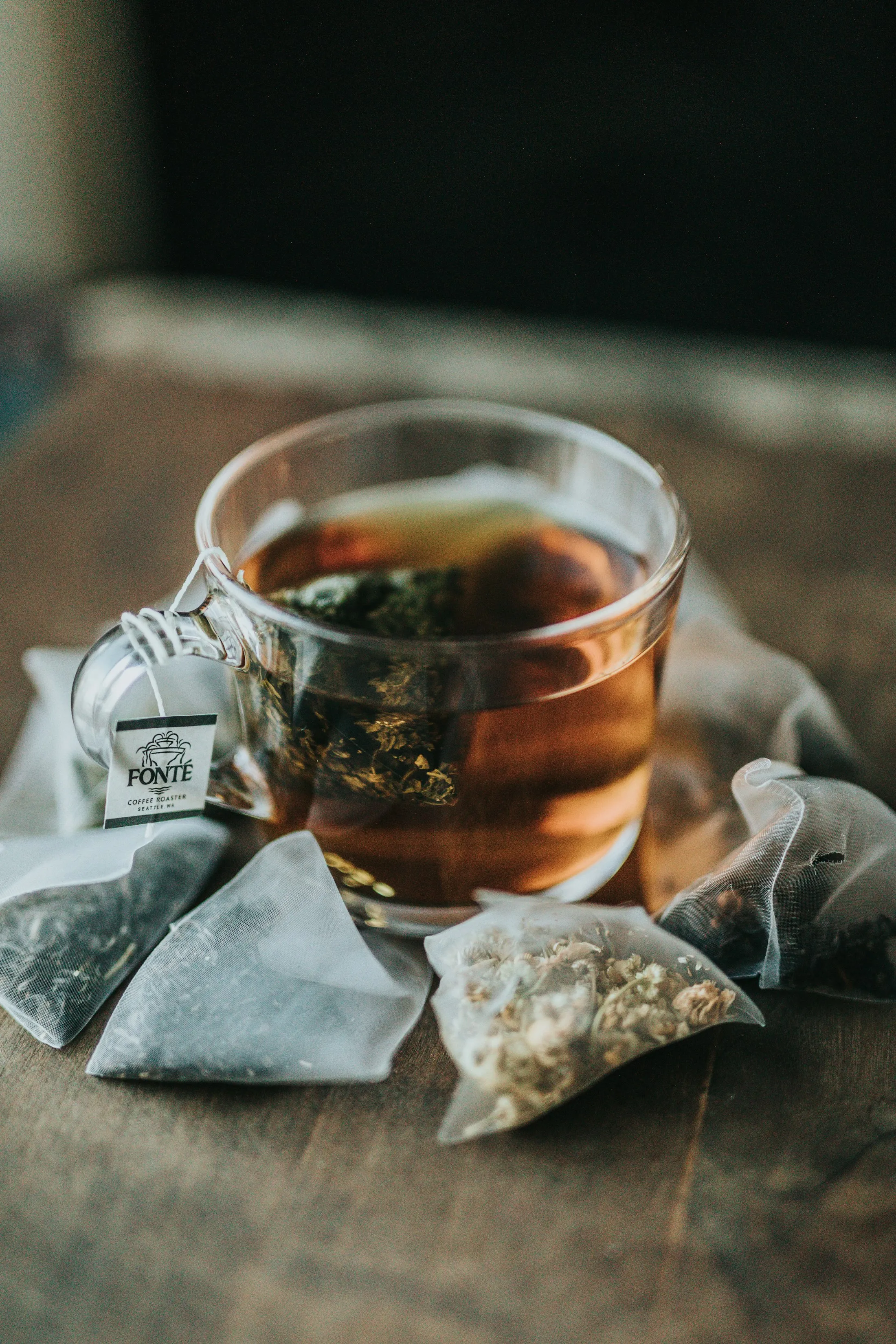 A clear glass cup of herbal tea on a wooden table with loose tea pouches around it