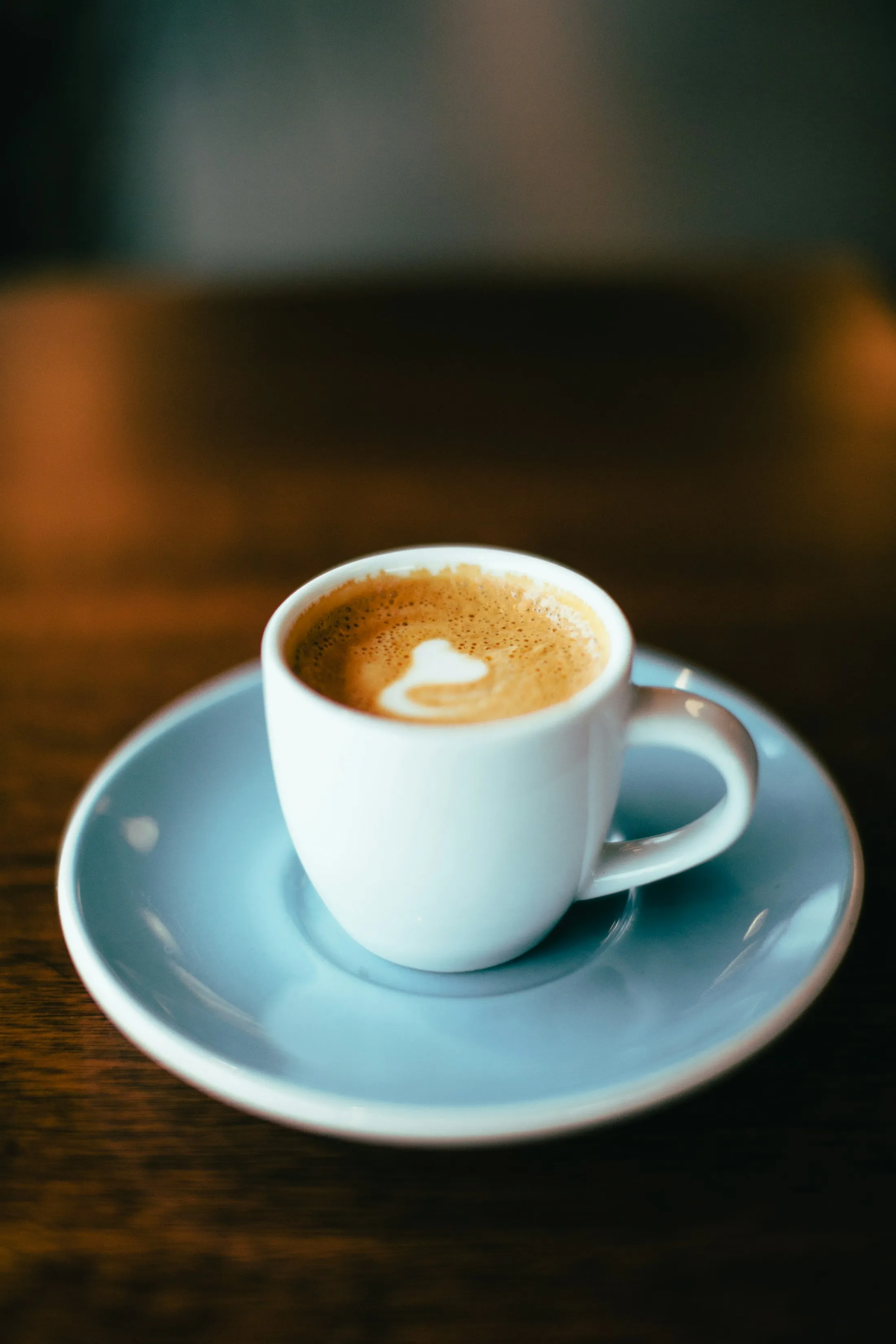 A small white espresso cup with latte art on a saucer
