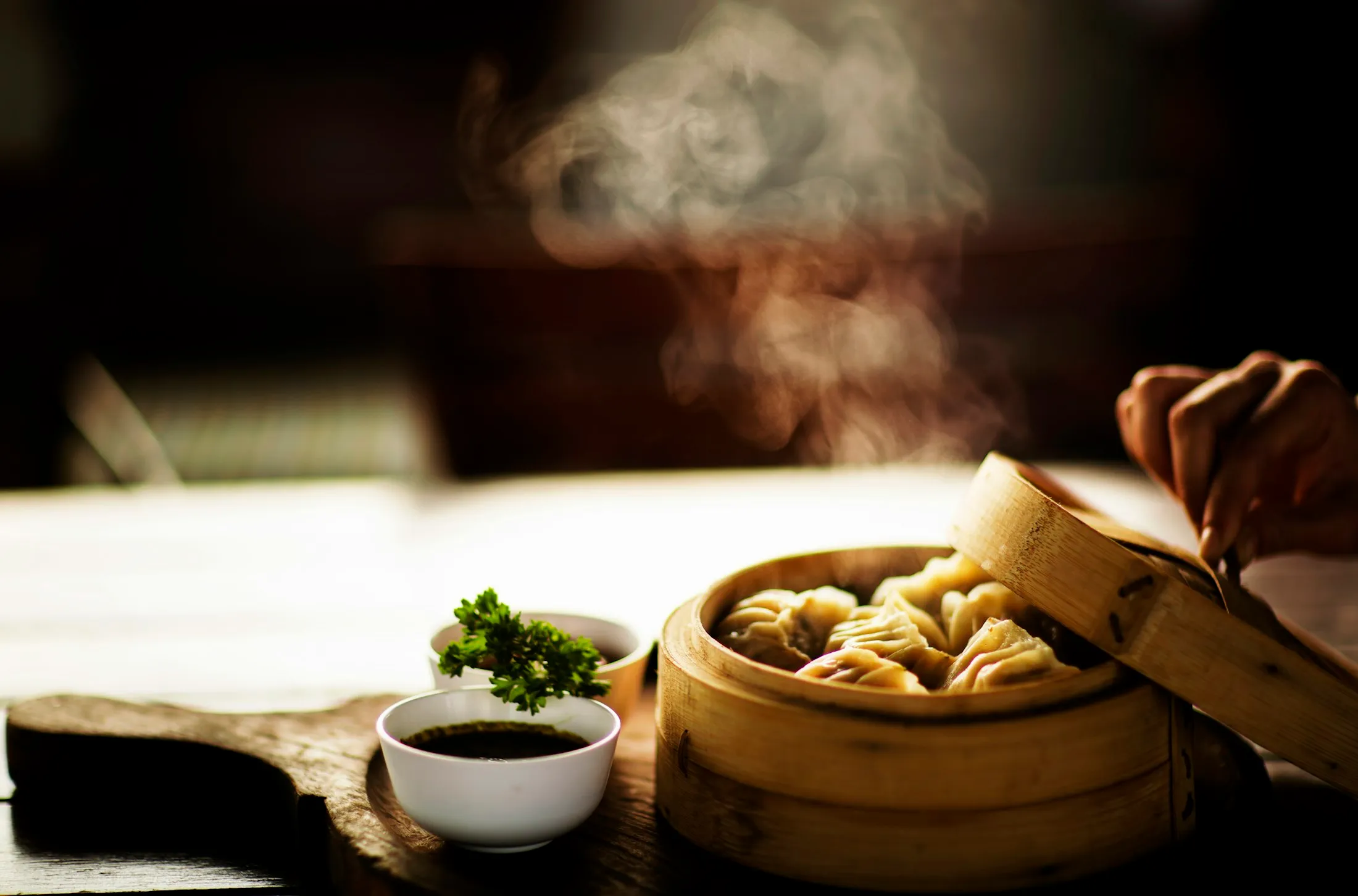 Steaming bamboo basket of momos with a small bowl of dipping sauce