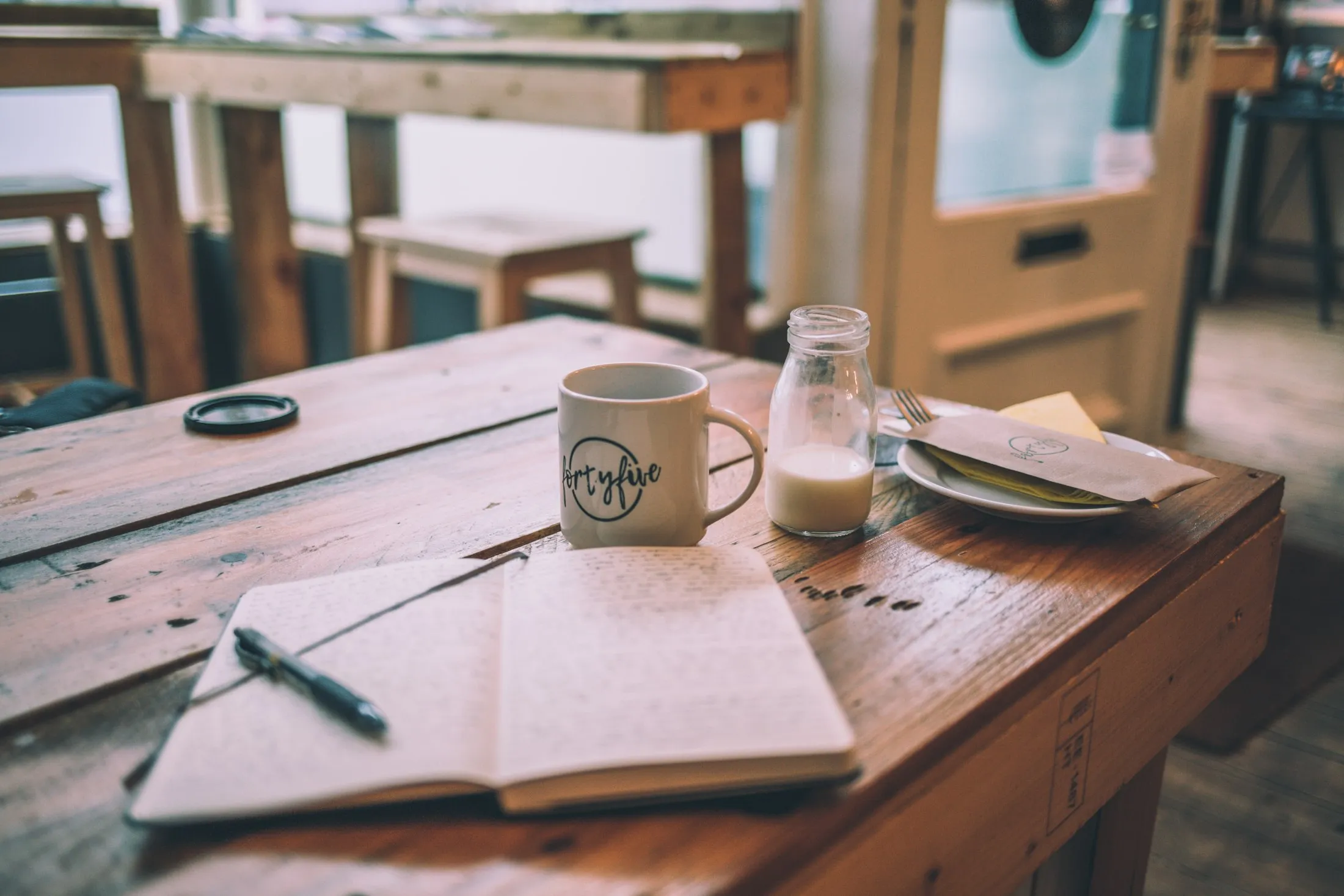 A coffee mug and an open notebook on a wooden cafe table
